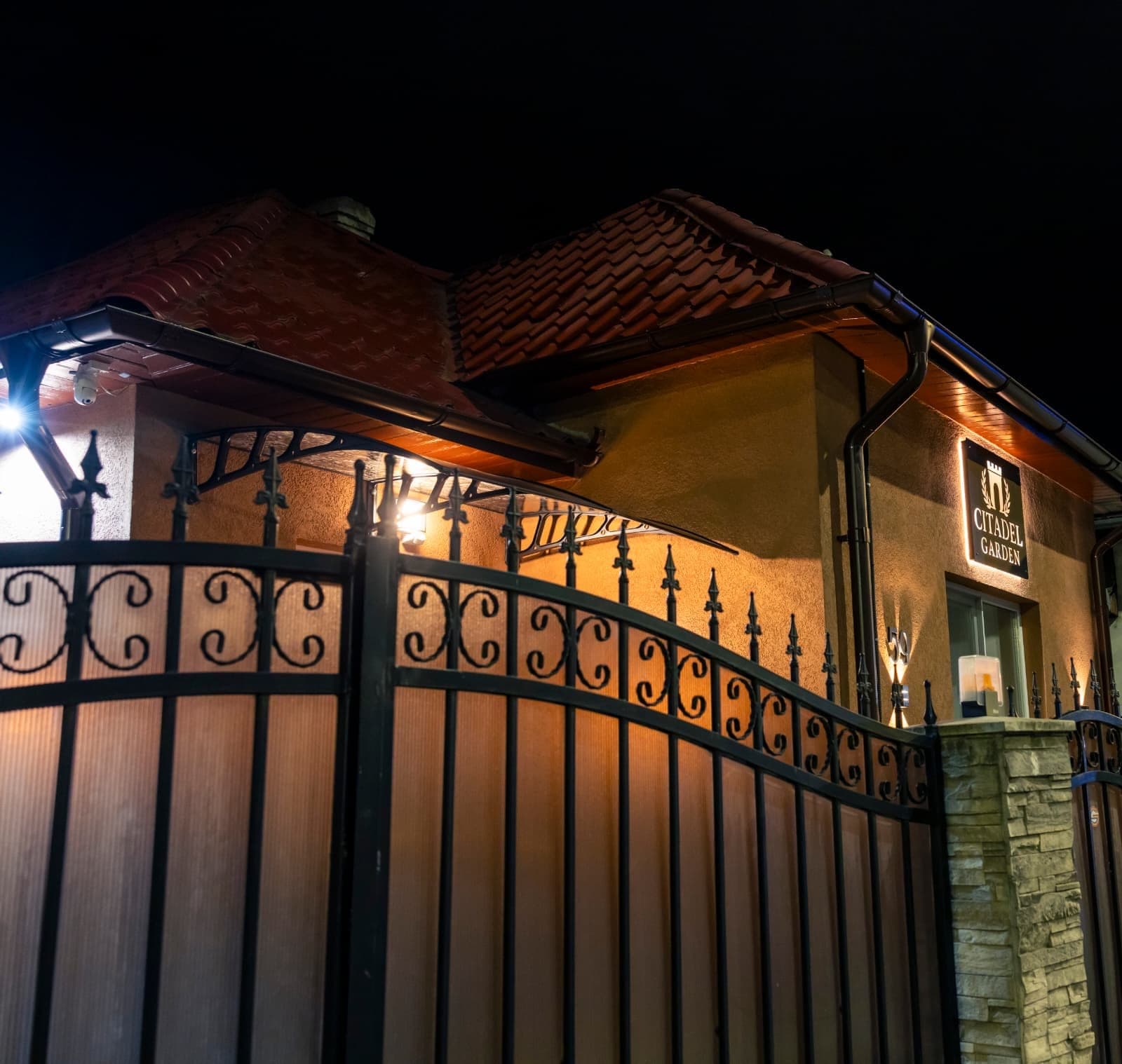Fațada Citadel Garden seara, cu poartă automată din fier forjat și firmă iluminată